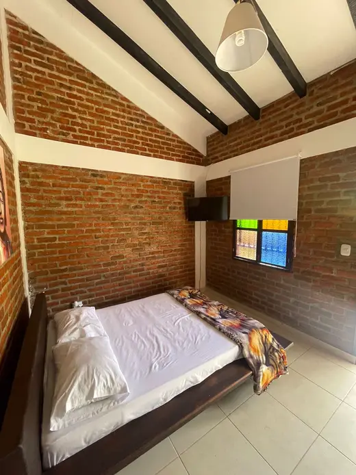 Habitación con cama de madera, pared de ladrillo y vitral de colores